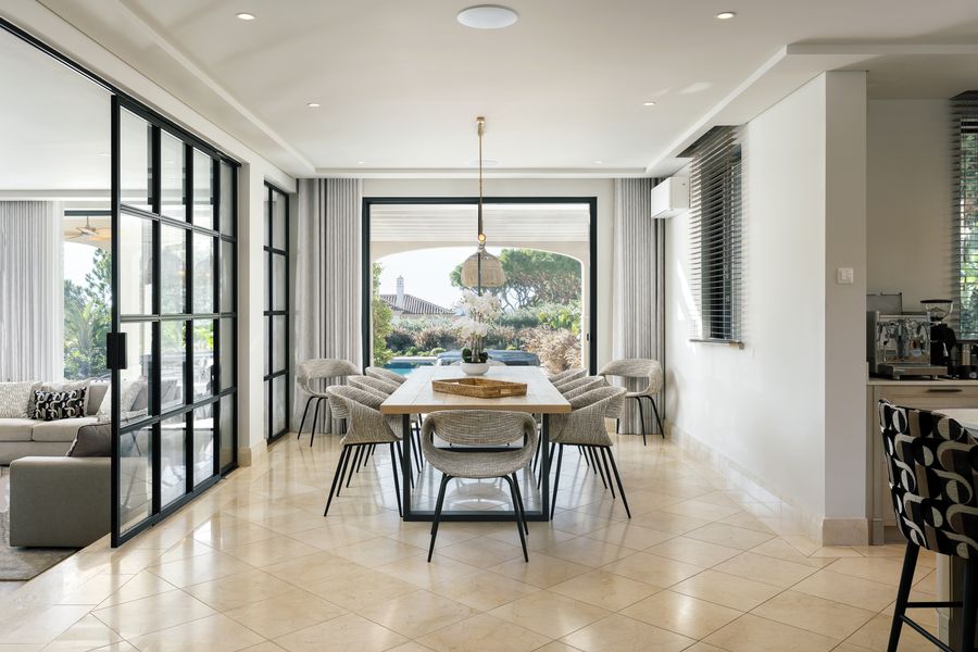 Dining table with woven chairs beside internal black-framed glazing — Dunas Douradas